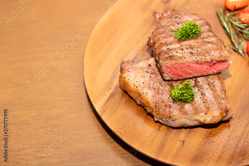 Fresh cooked half cut beef sirloin with cherry tomato and rosemary on top with parsley, Wood background, Copy space on the left