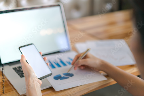 Business woman hand with Financial charts and mobile phone over laptop on the table .