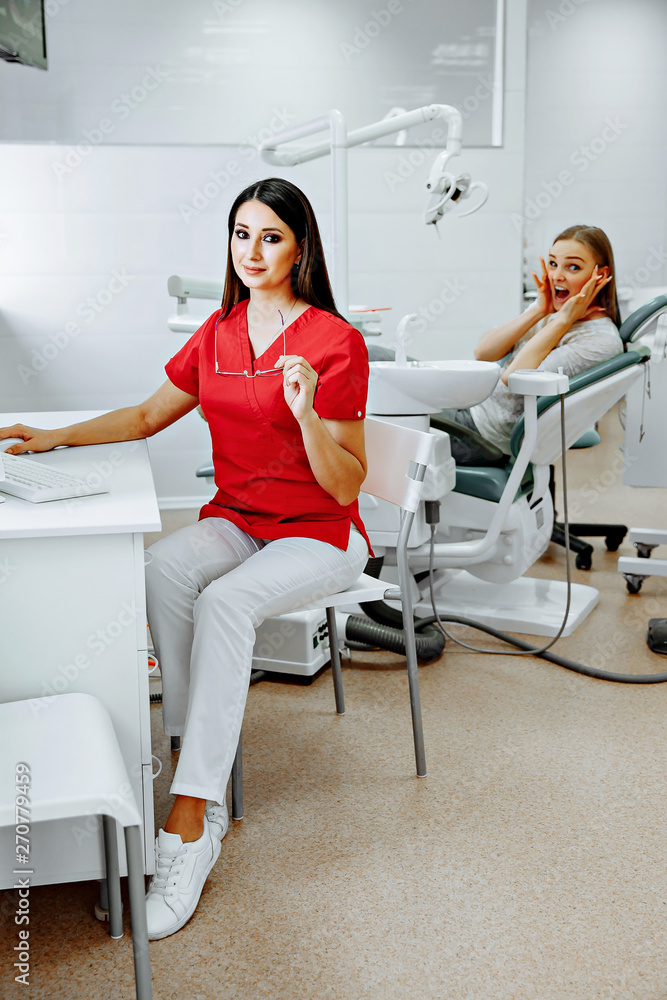 Blonde caucasian woman doctor in white uniform in clinic hospital works on computer and smiles at camera. Blonde caucasian woman doctor in white uniform in clinic hospital works on computer and smiles at camera.