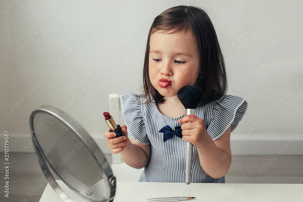 Beautiful girl does makeup. Little girl plays with her mother's makeup. Funny makeup baby. A woman of fashion paints her eyes and lips. A girl in a blue blouse at the mirror. 