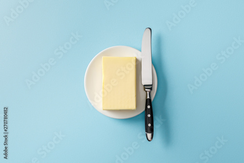 top view of butter and knife on white plate on blue background photo