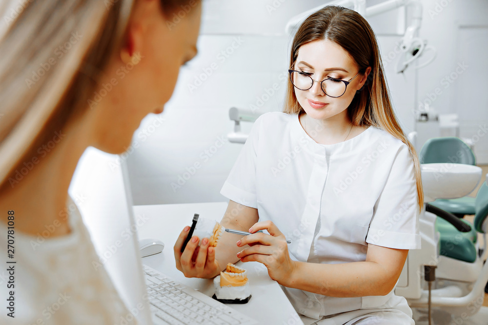 Concentrated dentist sitting at table and shows jaw samples tooth model to the patient Concentrated dentist sitting at table and shows jaw samples tooth model to the patient
