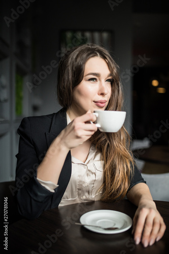 Beautiful smiling woman drinking coffee at cafe. Portrait of mature woman in a cafeteria drinking hot cappuccino and looking at camera. Pretty woman with cup of coffee.