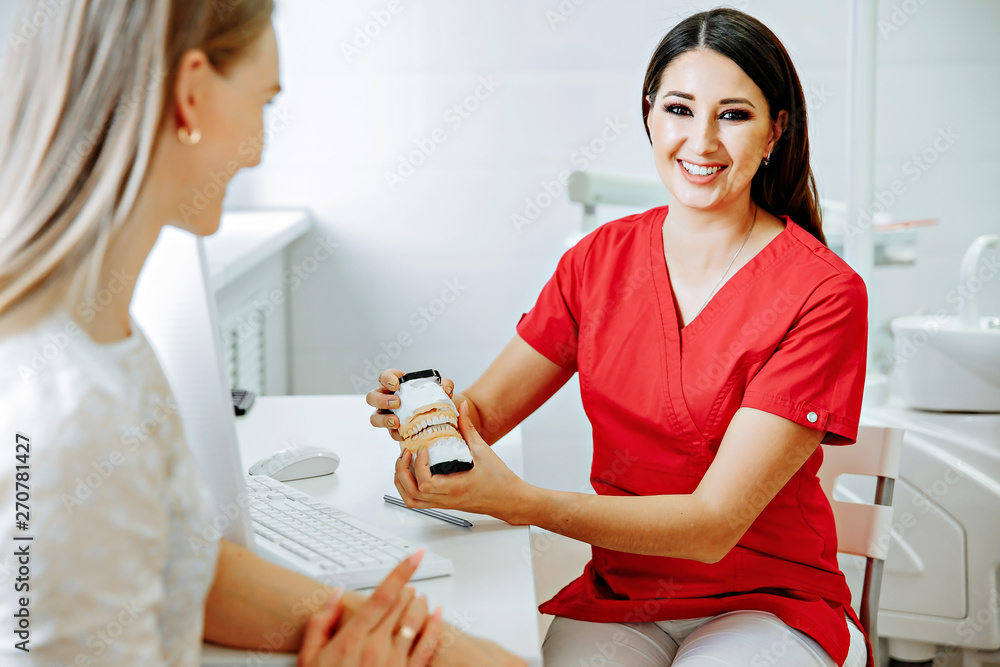 Concentrated dentist sitting at table and shows jaw samples tooth model to the patient Concentrated dentist sitting at table and shows jaw samples tooth model to the patient