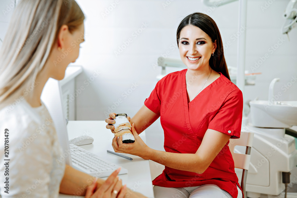 Concentrated dentist sitting at table and shows jaw samples tooth model to the patient Concentrated dentist sitting at table and shows jaw samples tooth model to the patient