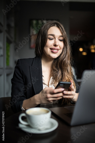 Smiling woman in cafe using mobile phone and texting in social networks.
