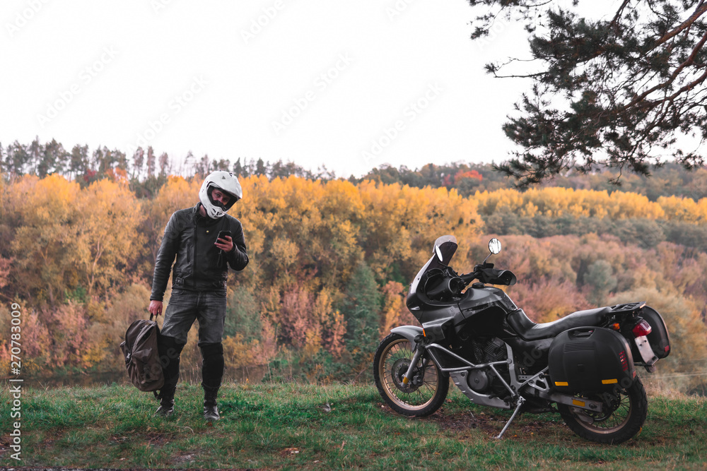 Fototapeta premium Rider standing with backpack. adventure motorcycle, Motorcyclist gear, A motorbike driver looks, concept of active lifestyle, enduro travel road trip. Evening, autumn. Tourist traveler. copy space