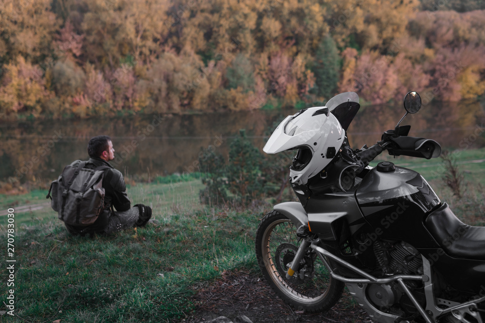 Obraz premium Lonley concept, man is sitting alone and look at the distance. Adventure motorcycle, Motorcyclist, A motorbike driver looks, concept of active lifestyle, enduro travel road trip, destination