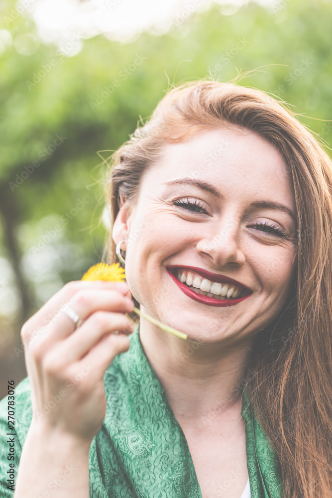 Frau, jung, 20-30, lächelnd, romantisch, genießt die ersten Sonnenstrahlen  im Frühling und hält einen Löwenzahn in der Hand. Stock Photo | Adobe Stock