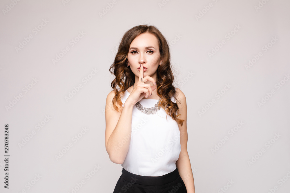 Beautiful pretty lady in white blouse decorated with silver accessory and black skirt posing at camera. Brunette woman holding finger near lips and asking being quite. Young girl not telling secrets. Beautiful pretty lady in white blouse decorated with silver accessory and black skirt posing at camera. Brunette woman holding finger near lips and asking being quite. Young girl not telling secrets.