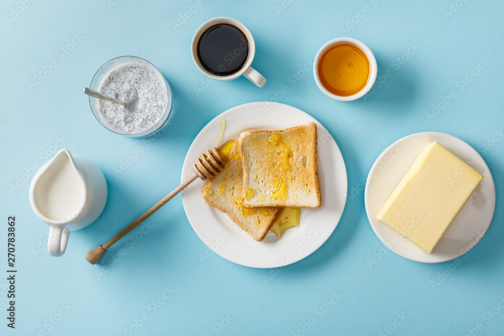 top view of coffee, milk, yogurt with chia seeds, butter, honey, toasts with honey and wooden dipper on white plates on blue background top view of coffee, milk, yogurt with chia seeds, butter, honey, toasts with honey and wooden dipper on white plates on blue background