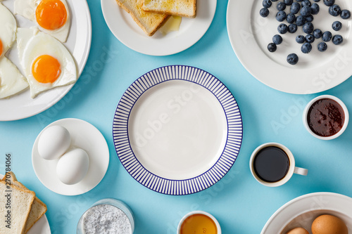 top view of served breakfast with empty plate in middle on blue background