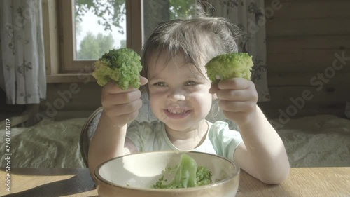Happy little girl hate eating broccoli vegetables on a plate with hands