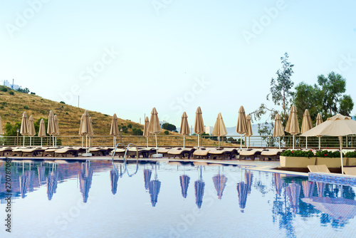 Outdoor luxury swimming pool, umbrellas, sun beds with reflection in the water at the holiday, background is beautiful mountain, relax place.