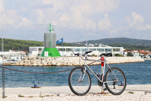 The bike is parked on the pier of the Mediterranean marina on the background of the signal beacon in green. Urban ecological mode of transport. Infrastructure Dalmatian Riviera. Vacation