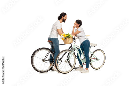 bearded latin man looking at attractive woman sitting on bicycle isolated on white