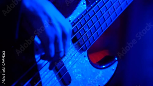Male musician playing bass guitar, shooting in a nightclub with artificial light, close-up and slow motion