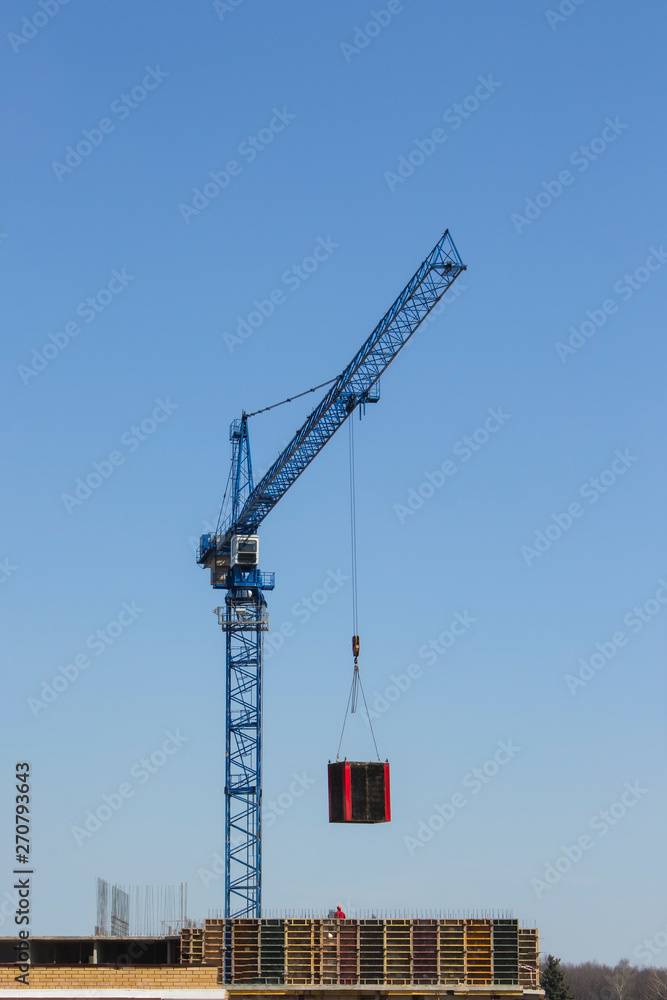 A construction crane moves the load. Building materials on pallets are moved by crane. Construction of a modern residential building