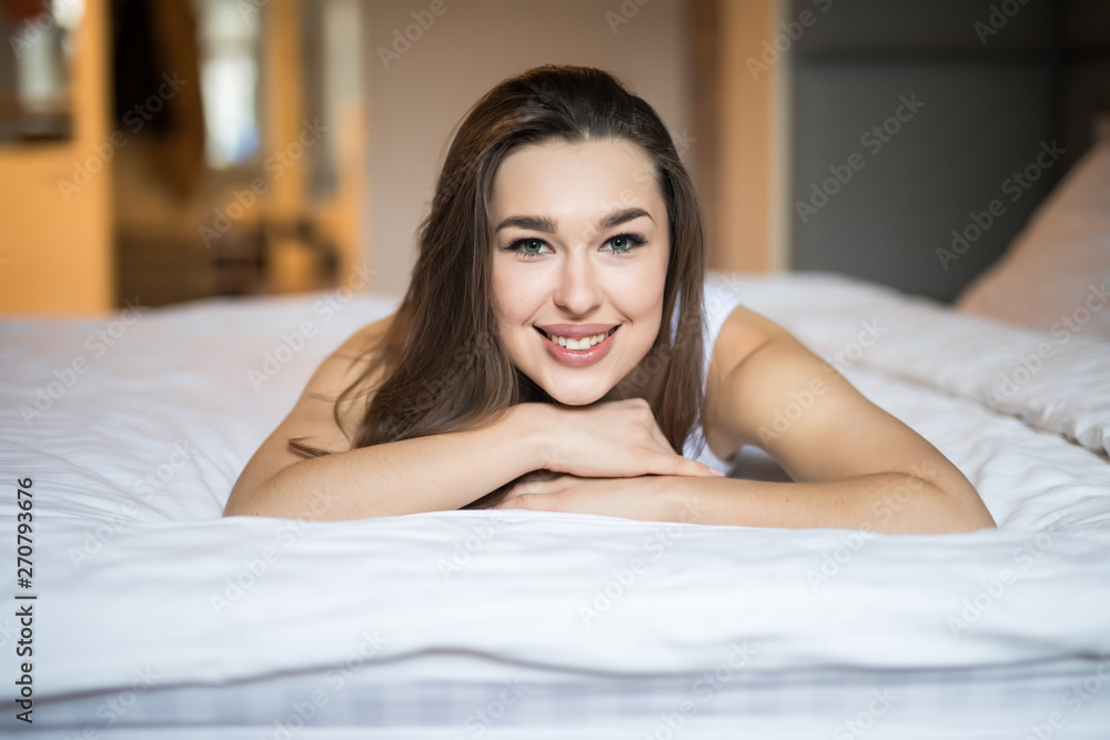 Young woman lying at the end of the bed and smiling, with her head resting upon her hand Young woman lying at the end of the bed and smiling, with her head resting upon her hand