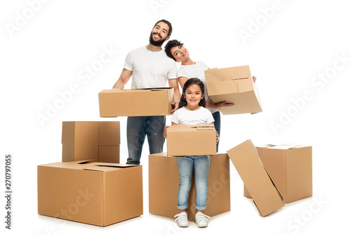 cheerful latin parents holding boxes and standing near cute daughter isolated on white