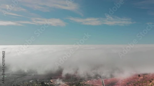 Aerial Hyperlapse Beautiful flight above the clouds over the red volcanic valley. In the frame of the mountain road hairpins serpentines are driven by cars. Mountainside with green plantations photo