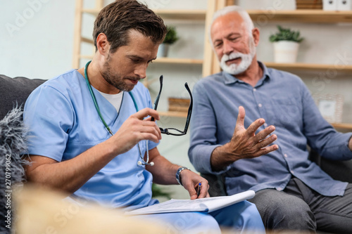 General practitioner analyzing medical documents of senior patient while being in home visit.