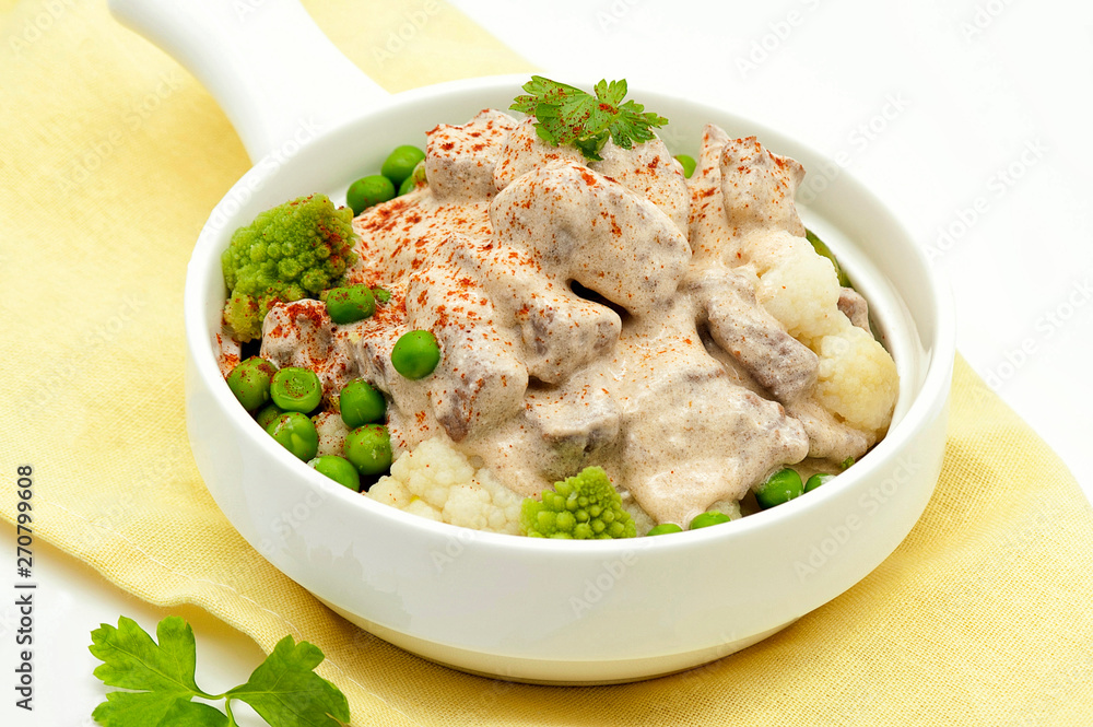 Fried meat stew in a creamy sauce and with a side dish of cabbage and green peas. In a portion of a white frying pan and on a yellow napkin. Close up and horizontal view Fried meat stew in a creamy sauce and with a side dish of cabbage and green peas. In a portion of a white frying pan and on a yellow napkin. Close up and horizontal view
