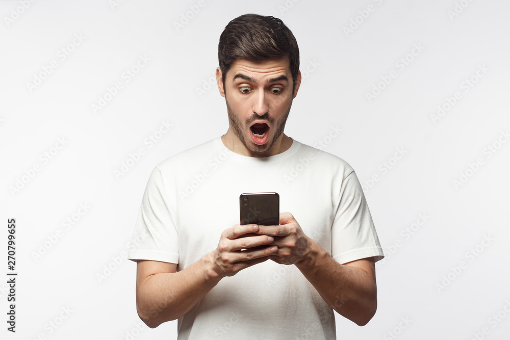Portrait of young man impressed by media content from web on display of her smartphone, isolated on gray background. Shock content concept Portrait of young man impressed by media content from web on display of her smartphone, isolated on gray background. Shock content concept