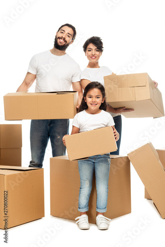 cheerful latin parents holding boxes and standing with cute daughter isolated on white