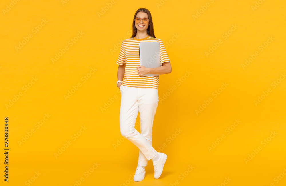 Young woman in casual clothes holding laptop, isolated on yellow background Young woman in casual clothes holding laptop, isolated on yellow background