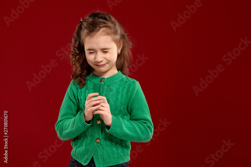 Portrait of a little brunette girl with a long, curly hair posing against a red background.