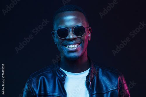 Studio shot of handsome smiling african american male model wearing trendy sunglasses and leather jacket