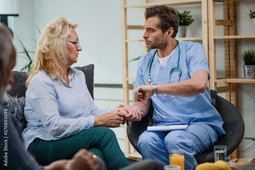 Healthcare worker checking pulse of mature patient while talking to her during a home visit. Healthcare worker checking pulse of mature patient while talking to her during a home visit.