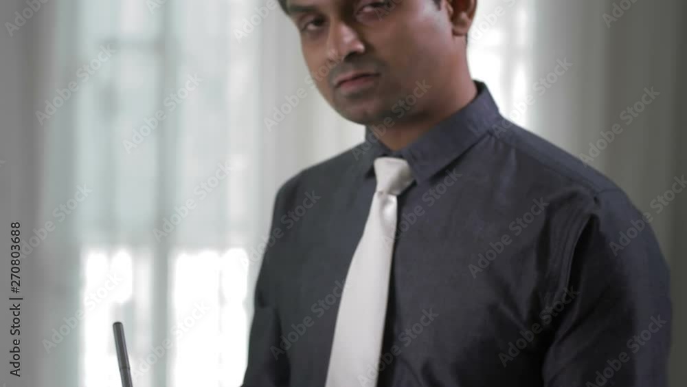 Tilt up of Indian businessman standing in office with papers in his hands and signing them Tilt up of Indian businessman standing in office with papers in his hands and signing them
