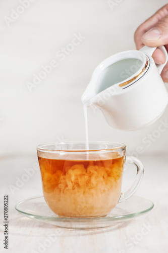 Milk poured into cup of tea by man hand