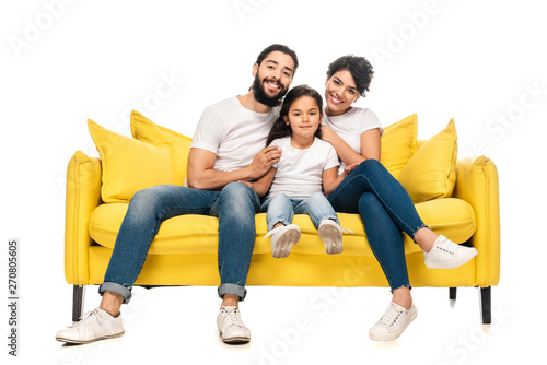 happy latin parents smiling while sitting on sofa with adorable daughter isolated on white