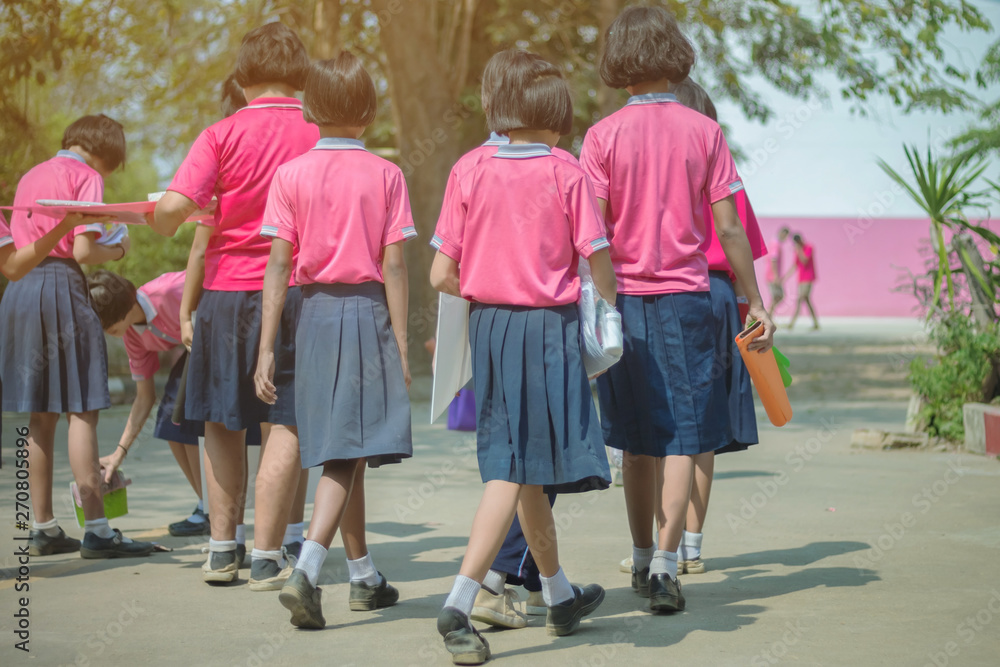 Obraz premium Back view of happiness primary girl students in pink shirt and blue skirt walk to classrooms with their friends.