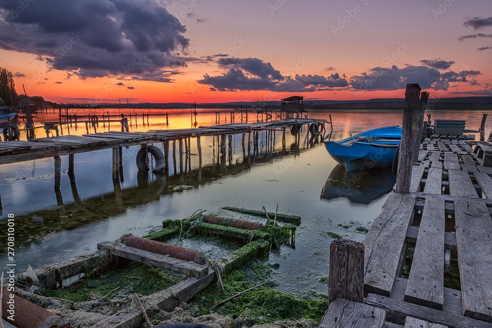 Fototapeta premium Exciting sunset on the harbor with wooden piers and boat. Horizontal view