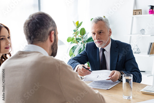 selective focus of car dealer in formal wear giving pen and contract to man near attractive woman