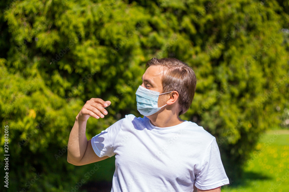 a man in a mask from allergy, in a white T-shirt, stands in the park a man in a mask from allergy, in a white T-shirt, stands in the park