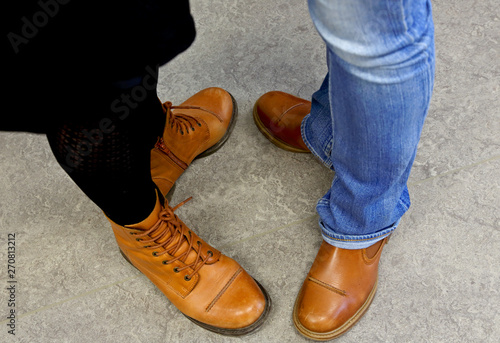 Two pair of feet with light brown leather boots on grey background