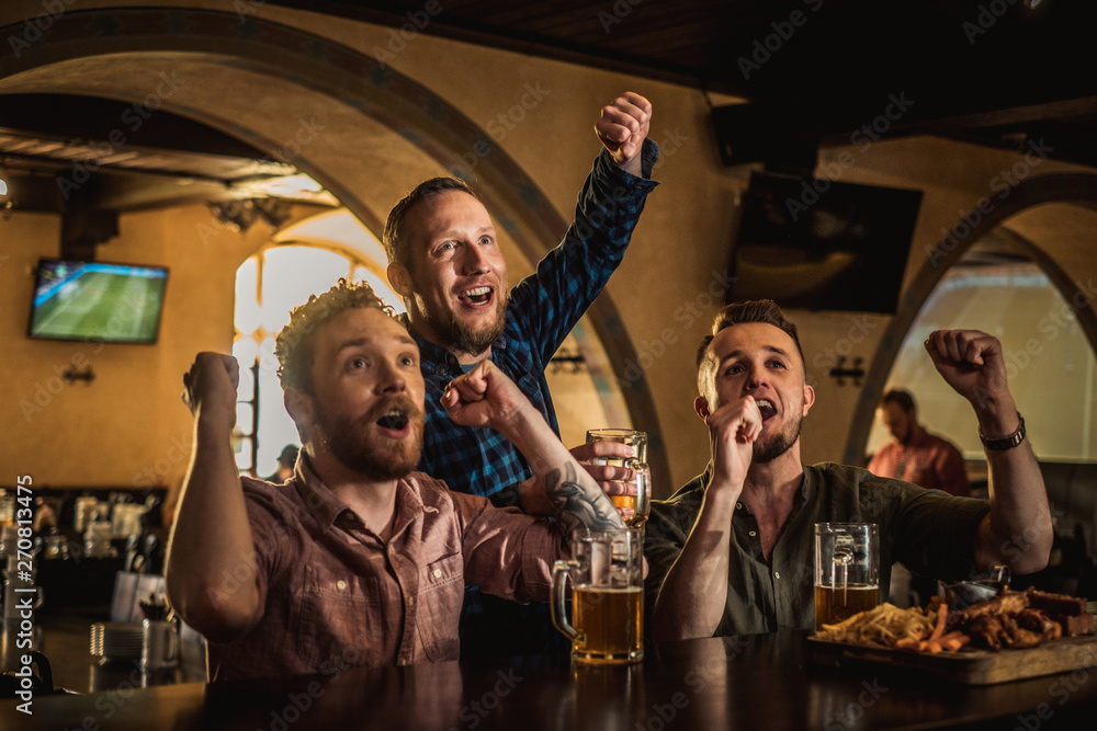 Fototapeta premium Friends drinking draft beer and watching tv in a pub