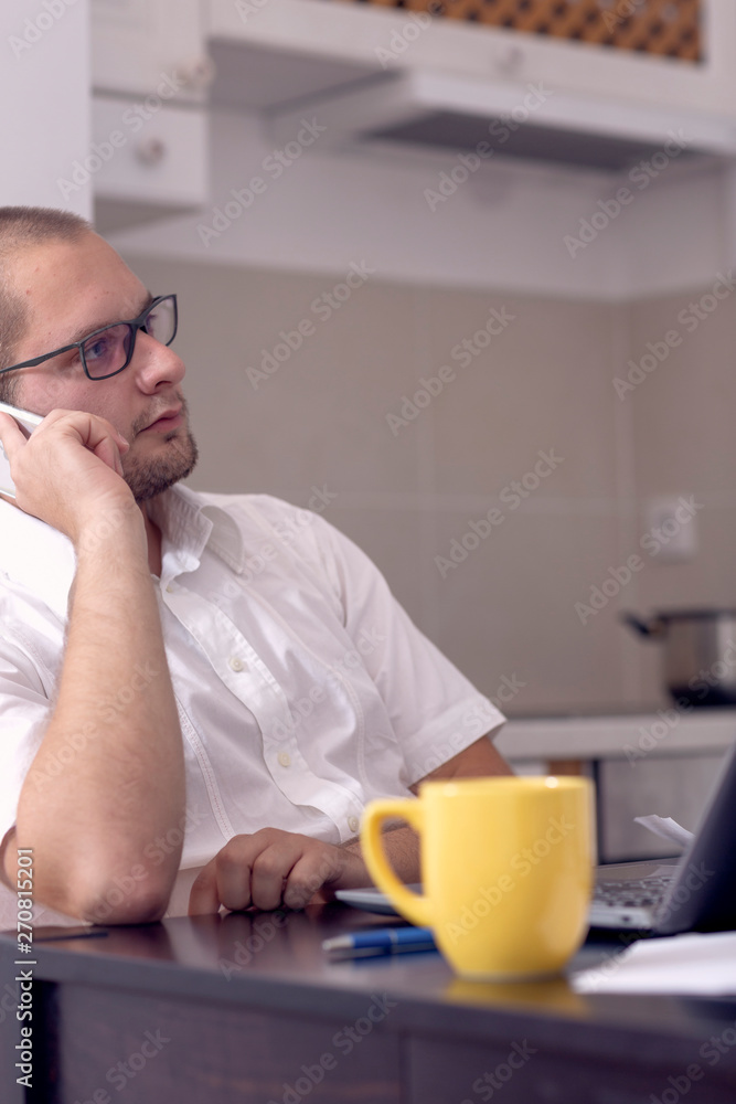 Young businessman working with computer while talking on phone at home. Young businessman working with computer while talking on phone at home.