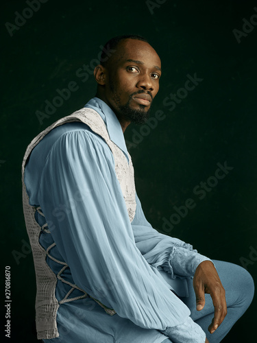 Obraz na plátně Young man as a medieval grandee or nobleman on dark studio background