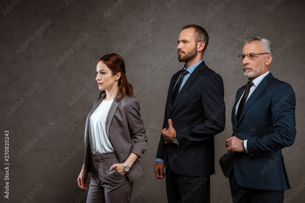 attractive businesswoman standing with hand in pocket near businessmen touching suits on grey attractive businesswoman standing with hand in pocket near businessmen touching suits on grey