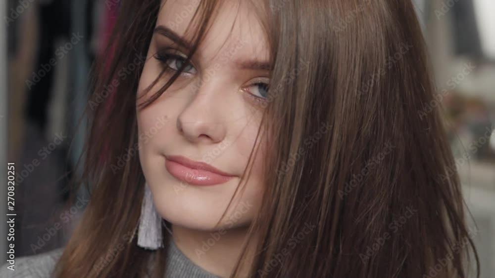 Closeup slow motion portrait of young beautiful brown haired woman with blue eyes adorable smile with natural makeup having fun in her room indoors looking at camera hair fluttering in the wind Closeup slow motion portrait of young beautiful brown haired woman with blue eyes adorable smile with natural makeup having fun in her room indoors looking at camera hair fluttering in the wind