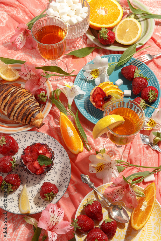 Appetizing breakfast, orange, croissant, strawberries and cakes on a red tablecloth. Top view.