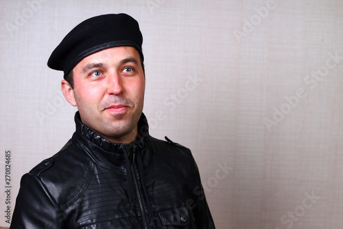 A cool rocker in a black leather jacket dreamily looks upwards on a blurred background of a wall in a studio. Emotion of creative inspiration