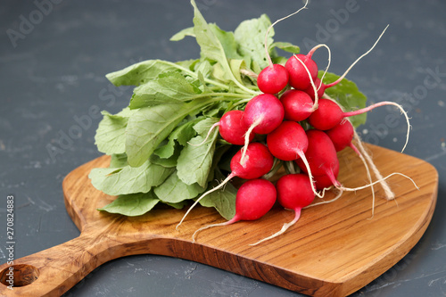Bouquet of radishes is located on a wooden board on a dark background, top view