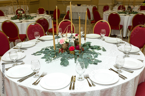 Festively decorated round banquet table in the restaurant. Fresh flowers are golden candles and red chairs. expensively rich